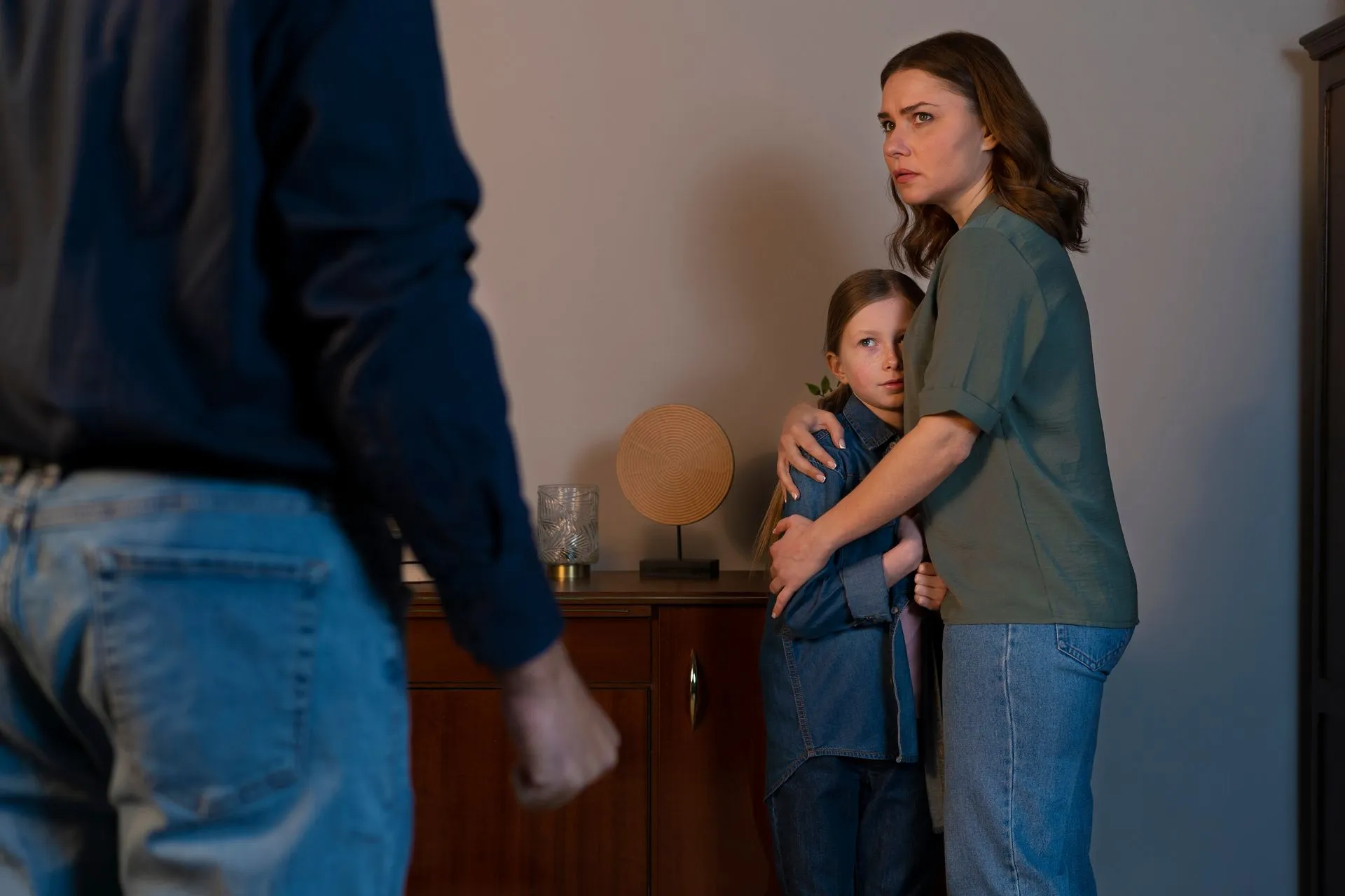Man faces family. Woman and child look worried, indoors.